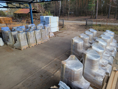 Stacks of wrapped greenhouses on pallets outdoors with a forest background